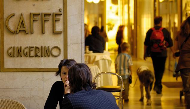 Persone parlano davanti al Caffè Gingerino a Bolzano, sullo sfondo passanti sotto i portici.